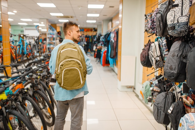 Uomo che sceglie uno zaino, shopping nel negozio di articoli sportivi. Stile di vita estremo stagione estiva, negozio per il tempo libero attivo, clienti che acquistano attrezzature turistiche