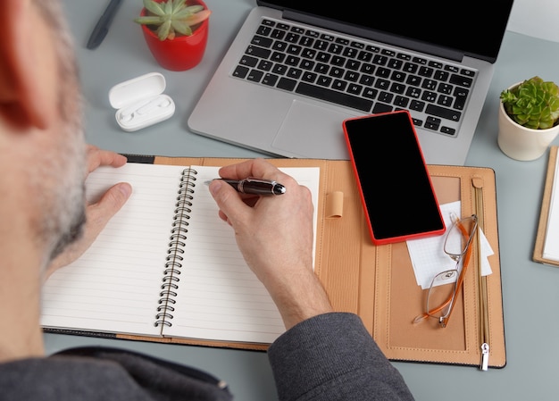 Uomo che scrive nell'agenda vicino al computer portatile da vicino. Concetto di affari. Modello di telefono