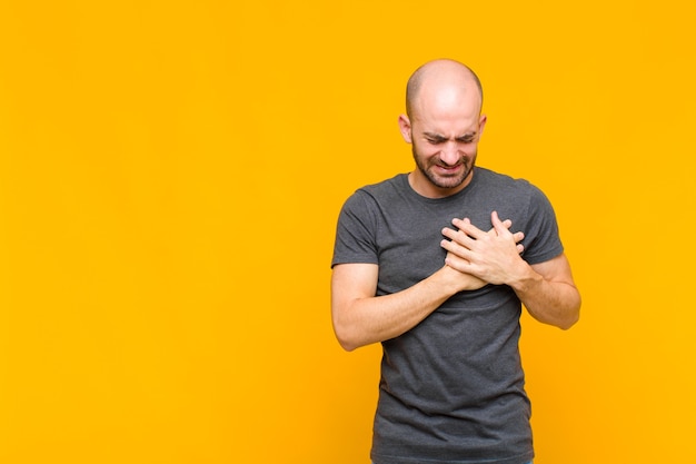 Uomo che sembra triste, ferito e affranto, tenendo entrambe le mani vicino al cuore, piangendo e sentendosi depresso