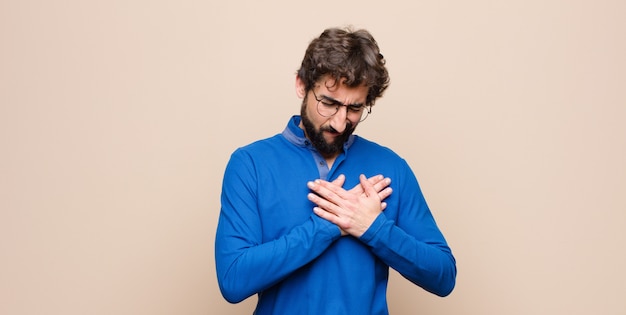 Uomo che sembra triste, ferito e con il cuore spezzato, tenendo entrambe le mani vicino al cuore, piangendo e sentendosi depresso