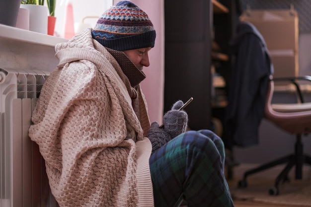 Uomo che sente freddo a casa che ha problemi con il riscaldamento domestico seduto con il telefono. Niente soldi per pagare il servizio