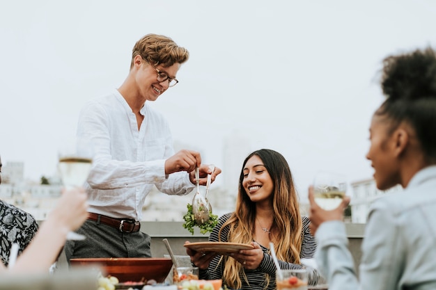 Uomo che serve insalata di amici a una festa sul tetto