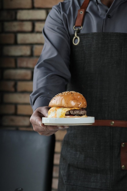 Uomo che serve un grande panino con hamburger di manzo con un uovo fritto al suo interno all'interno di un lussuoso ristorante