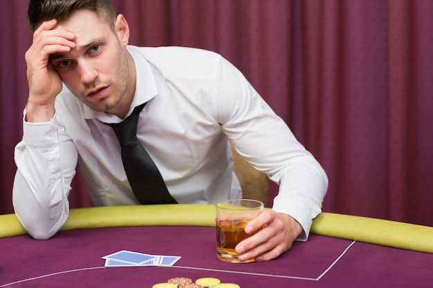 Uomo che si appoggia sul tavolo da poker bevendo whisky