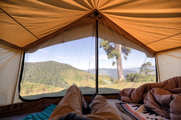 Uomo che si distende in una tenda sulla collina con cielo blu in campagna