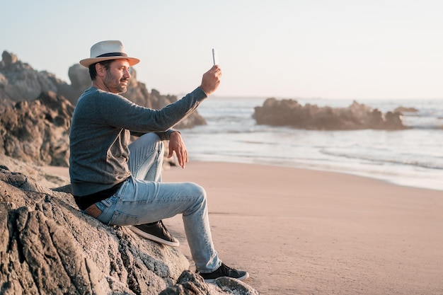 Uomo che si fa selfie con lo smartphone e sorride felice sulla spiaggia