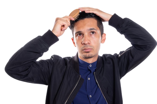 Uomo che si pettina i capelli isolato su sfondo bianco Giovane uomo latino con pettine di legno nei capelli