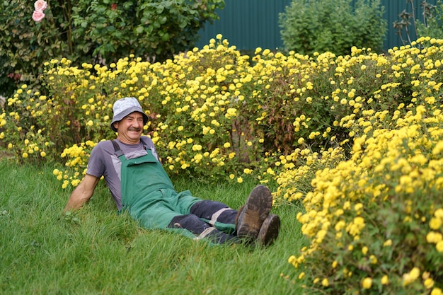 Uomo che si rilassa sull'erba con cespugli di fiori gialli sullo sfondo Maschio bello che riposa sull'erba e si gode una giornata di sole in crisantemi in fiore