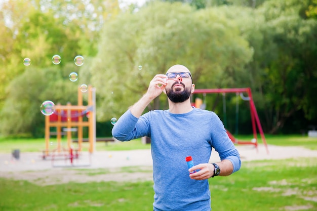 Uomo che soffia bolle di sapone nel parco vicino al parco giochi.