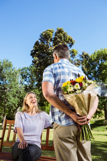 Uomo che sorprende la sua ragazza con un mazzo di fiori nel parco