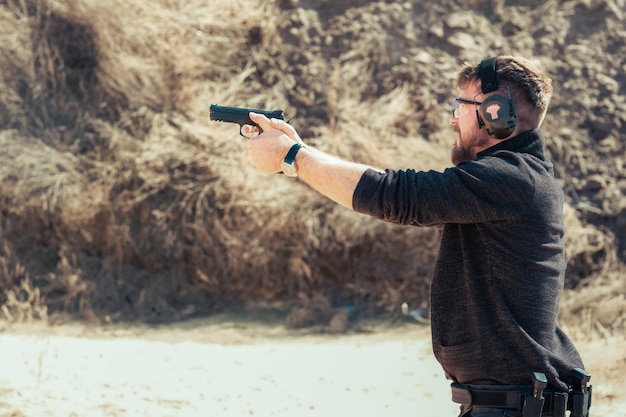 Uomo che spara con una pistola in allenamento con protezione da rumore e occhiali su uno sfondo di muro di pietra