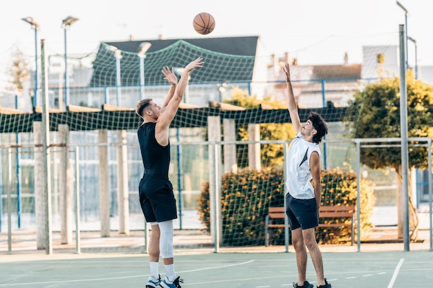 Uomo che spara da tre punti durante una partita di basket tra amici su un campo urbano all'aperto.