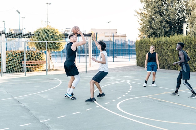 Uomo che spara la palla al canestro durante una partita di basket in un campo urbano tra amici