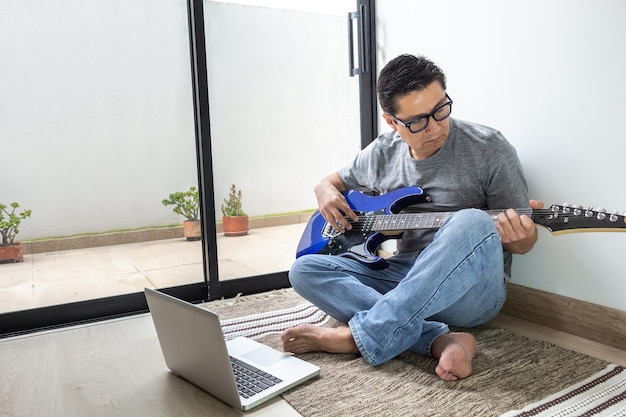 Uomo che suona la chitarra elettrica davanti al suo computer a casa