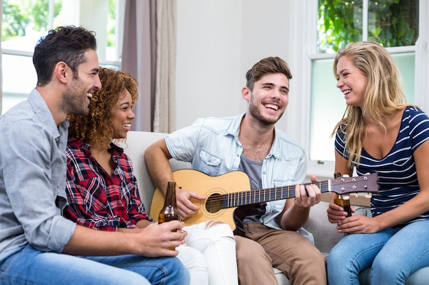 Uomo che suona la chitarra mentre amici che godono della birra