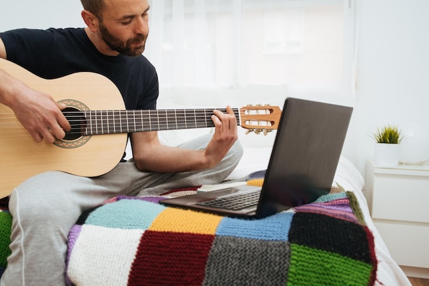 Uomo che suona la chitarra mentre guarda il portatile