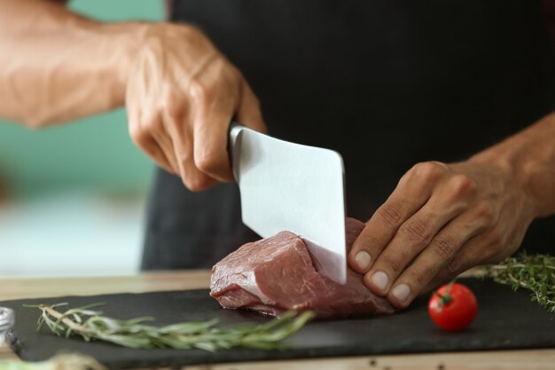Uomo che taglia carne cruda su lastra di ardesia in cucina
