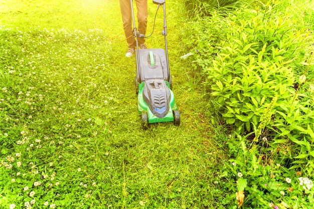 Uomo che taglia erba verde con tosaerba in cortile. Fondo di stile di vita del paese di giardinaggio