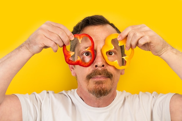 Uomo che tiene fette di peperoni rossi e gialli sugli occhi come occhiali da vista