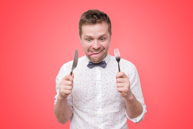 Uomo che tiene forchetta e coltello a portata di mano pronto da mangiare leccandosi le labbra