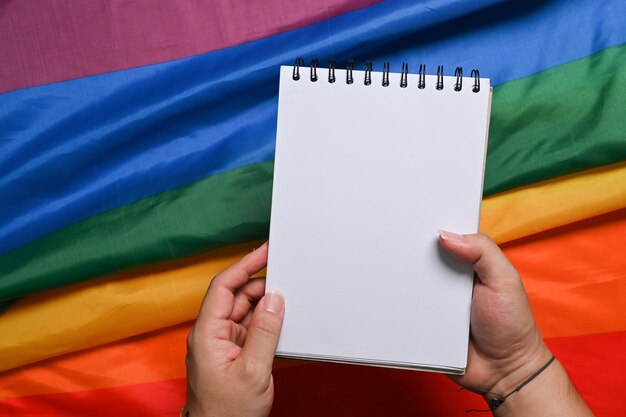 Uomo che tiene il blocco note vuoto sopra la bandiera arcobaleno Lgbt colorato.