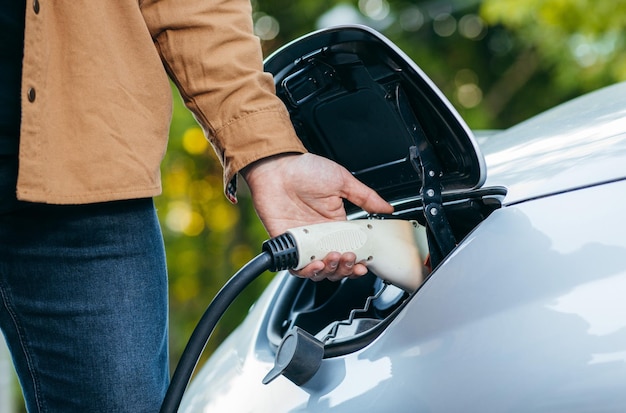 Uomo che tiene il cavo di alimentazione alla stazione di ricarica per veicoli elettrici Primo piano