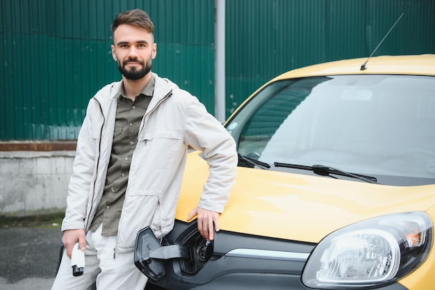 Uomo che tiene il cavo di ricarica per auto elettrica nel parcheggio all'aperto e collegherà l'auto alla stazione di ricarica nel parcheggio vicino al centro commerciale