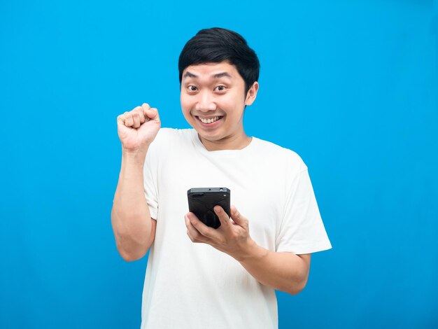 Uomo che tiene il cellulare gesto felice mostra pugno su sfondo blu