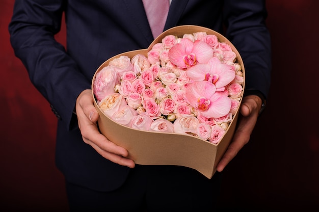 Uomo che tiene in una mano una scatola rosa di orchidee, rose e peonie