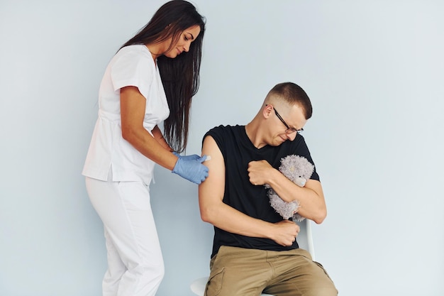 Uomo che tiene l'orsacchiotto durante la procedura Medico in uniforme che effettua la vaccinazione al paziente