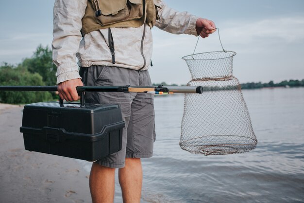 uomo che tiene la rete da pesca e scatola nera di plastica in mano. Anche lui ha la mosca in quella giusta. Guy è in piedi sulla riva del watr.