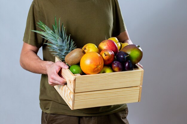 Uomo che tiene la scatola di legno piena di frutta fresca su bianco