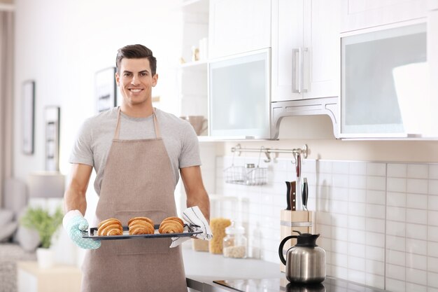 Uomo che tiene la teglia con deliziosi croissant fatti in casa in cucina