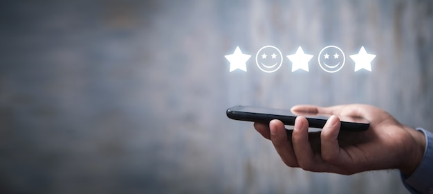 Uomo che tiene smartphone con una faccia sorridente e stelle. Feedback. Soddisfazione del cliente