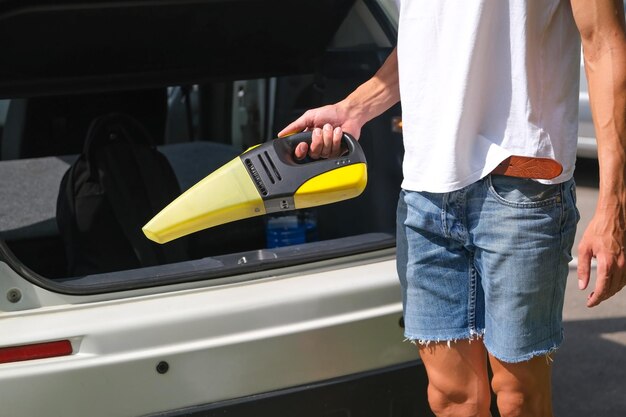 uomo che tiene un pratico aspirapolvere sullo sfondo dell'auto