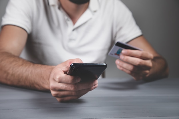 Uomo che tiene un telefono e una carta di credito. concetto di acquisto online sul muro grigio