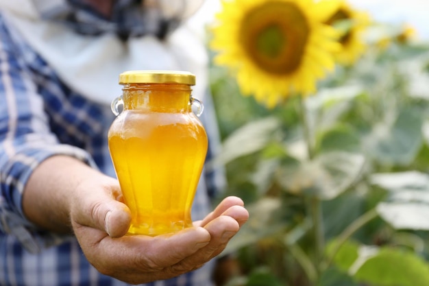 Uomo che tiene una bottiglia di miele su sfondo di campo di girasole