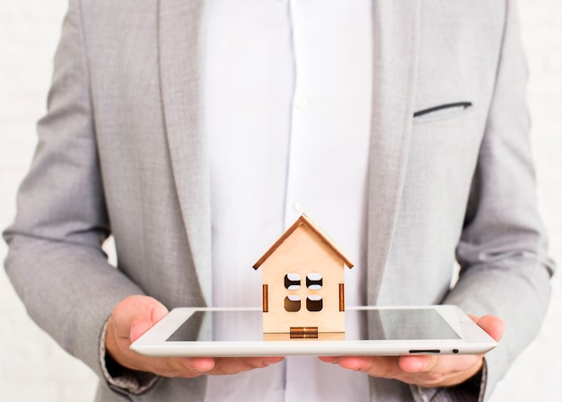 Uomo che tiene una casa di legno su un tablet