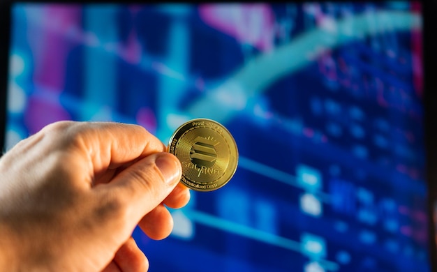 Uomo che tiene una moneta Solana dorata con il grafico del mercato azionario finanziario sullo sfondo Moneta di criptovaluta Mercato finanziario