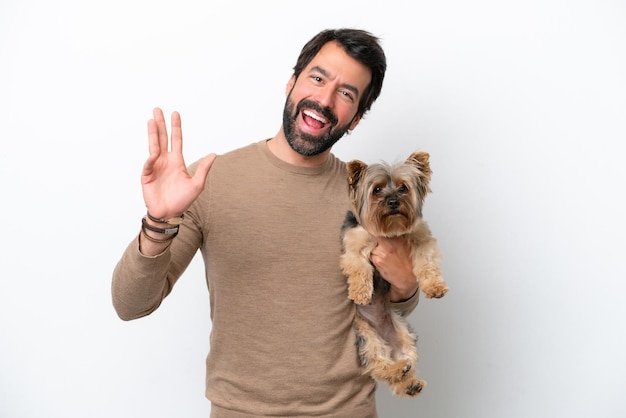 Uomo che tiene uno Yorkshire isolato su sfondo bianco salutando con la mano con un'espressione felice