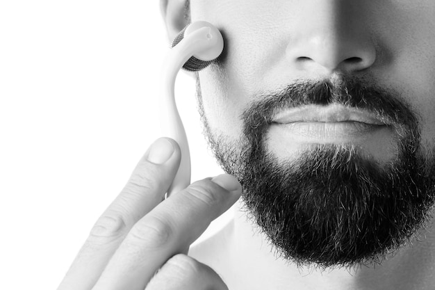 Uomo che usa il rullo meso per una migliore crescita della barba su sfondo bianco