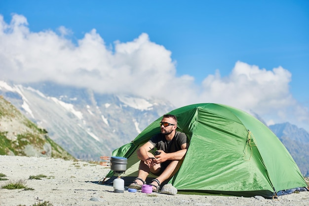 Uomo che usa la radio vicino alla tenda in montagna