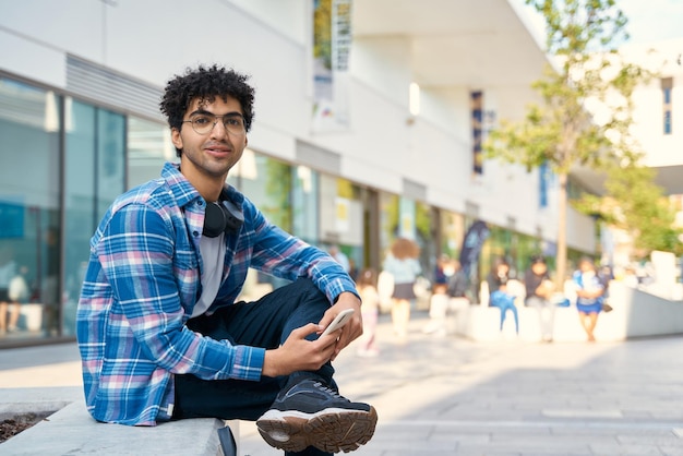 Uomo che usa lo smartphone mentre è seduto da solo per la strada della città