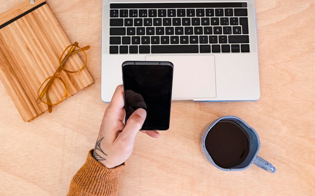 uomo che usa uno smartphone e un portatile con una tazza di caffè Closeup