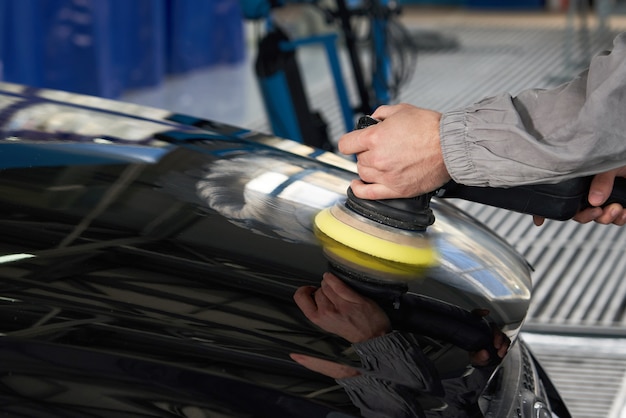 Uomo che usando lucidatore per lucidare la carrozzeria nera in officina