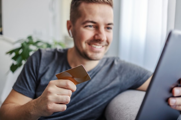 Uomo che utilizza carta di credito e tablet per lo shopping online mentre è seduto a casa