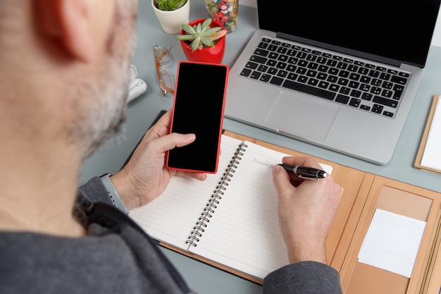 Uomo che utilizza il cellulare e scrive LUNEDI' nell'agenda vicino al laptop da vicino. Concetto di affari