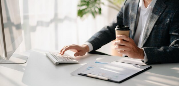 Uomo che utilizza il computer portatile e digita sul computer portatile e tiene in mano una tazza di caffè nell'home office del bar