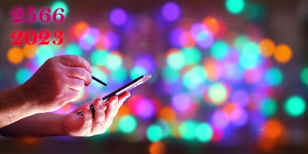 Uomo che utilizza il telefono cellulare per augurare il nuovo anno su sfocatura sfondo astratto multi colore bokeh