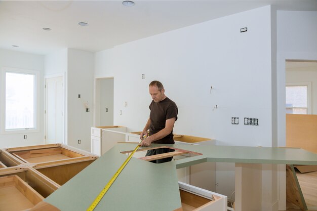 Uomo che utilizza la misura di nastro per la misurazione della dimensione del controsoffitto di legno nella cucina moderna per il miglioramento domestico.